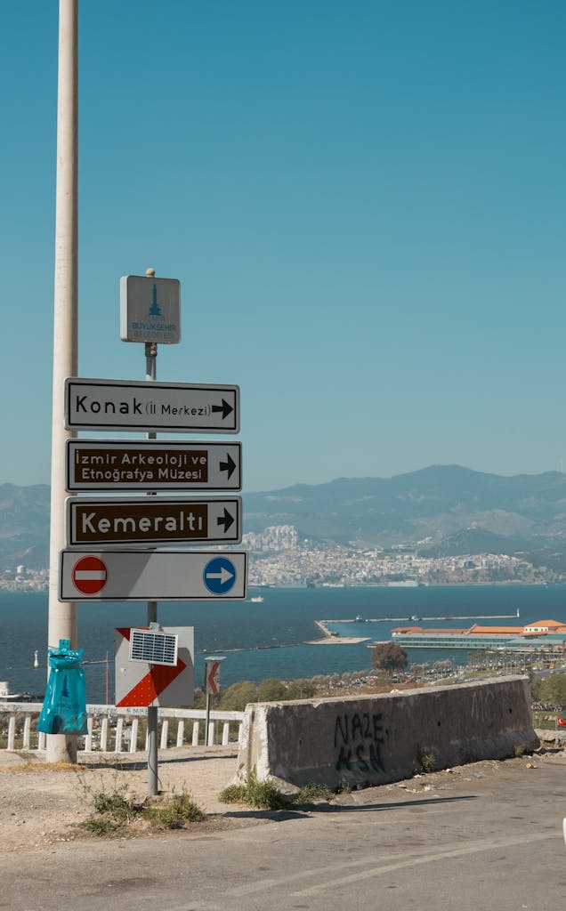 Street signs pointing to landmarks with Izmir coastal view in Turkey.